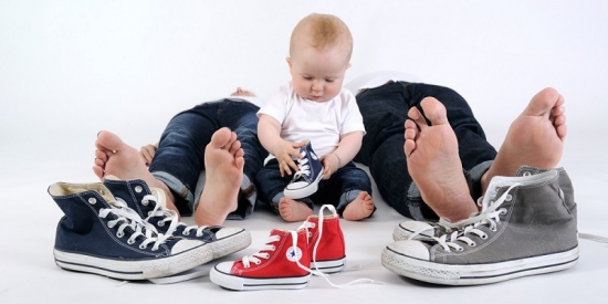 Baby sitzt zwischen den Füßen der Eltern inmitten von Schuhen