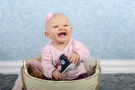 Baby sitzt lachend in einer Wann und hält einen Schuh in der Hand