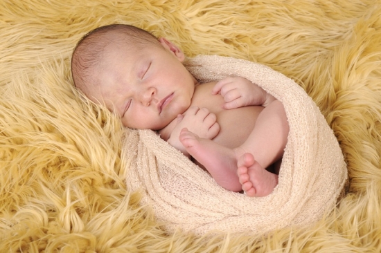 Neugeborenes Baby schläft zusammengerollt in einem Tuch